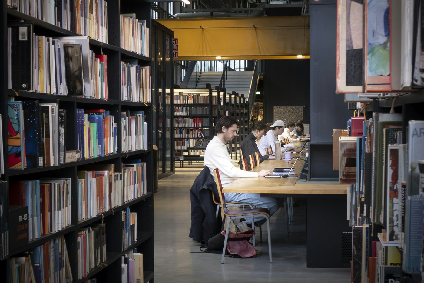 People studying at tables between the shelves of a public library