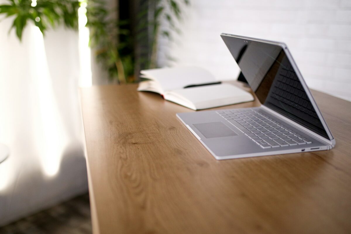 An open laptop and notebook on a wooden table in window light
