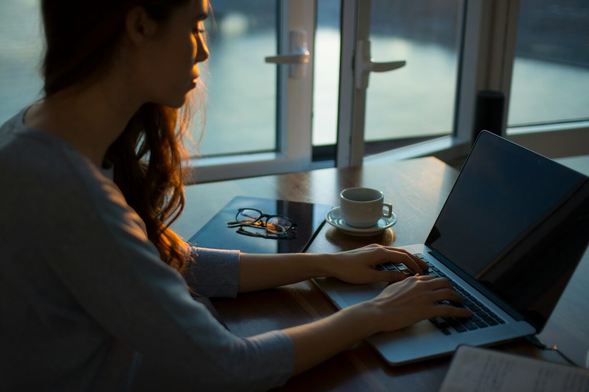 A woman working through email at a laptop by a window